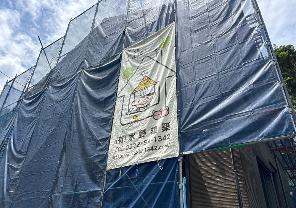 Construction site wrapped in blue tarps with a vertical banner showing a cartoon house and a cat under a roof.