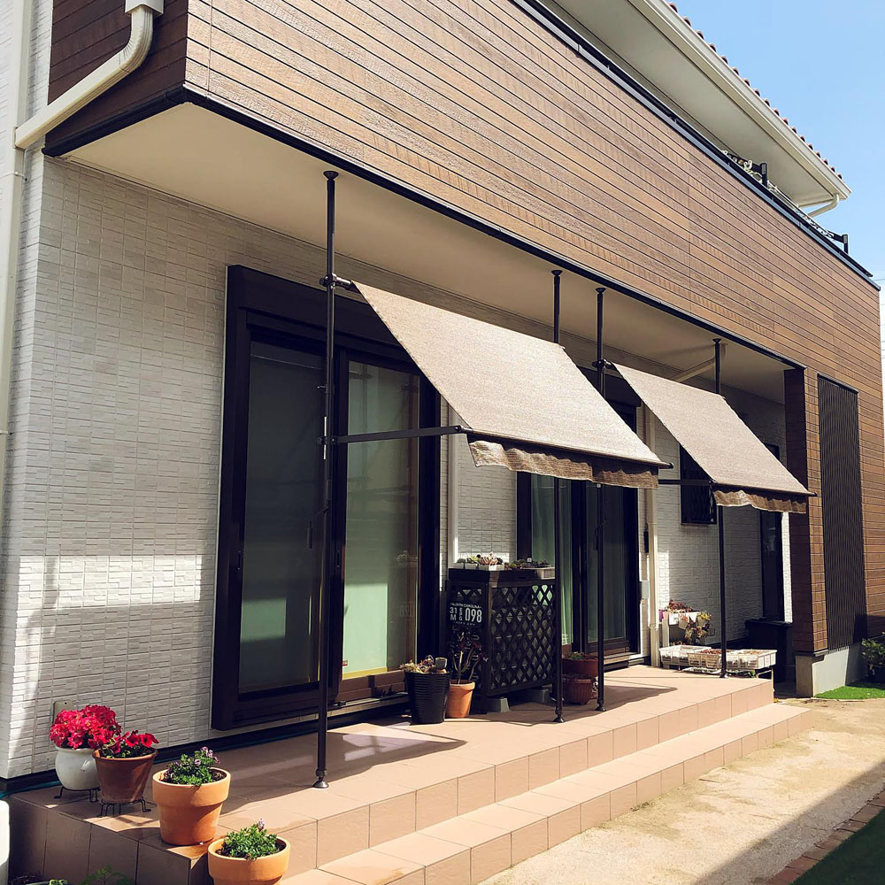 Front of a modern house with two beige fabric awnings over sliding doors; potted plants line the tiled steps.