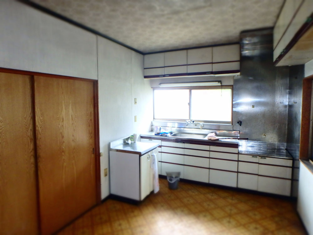 Old-fashioned kitchen with white cabinets, wooden sliding doors, and a stainless steel sink under a window.