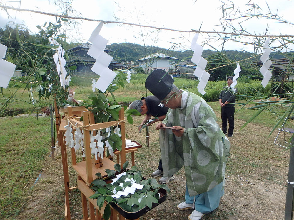 Outdoor Shinto ritual: a priest in traditional robes bows over an offering at a wooden altar with shide paper and greenery
